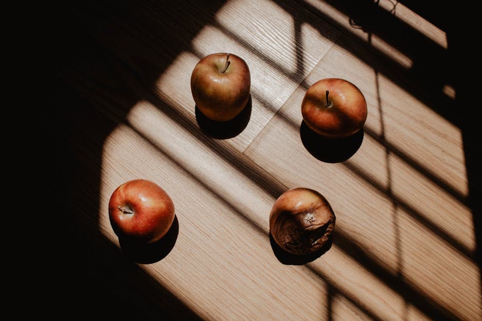 Four apples on warm wood with dramatic window-blind shadow stripes