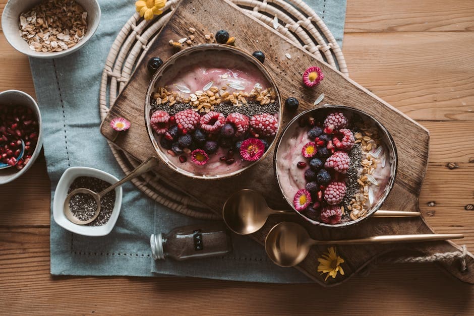 Two smoothie bowls overhead with berries chia seeds granola pomegranate on sage napkin