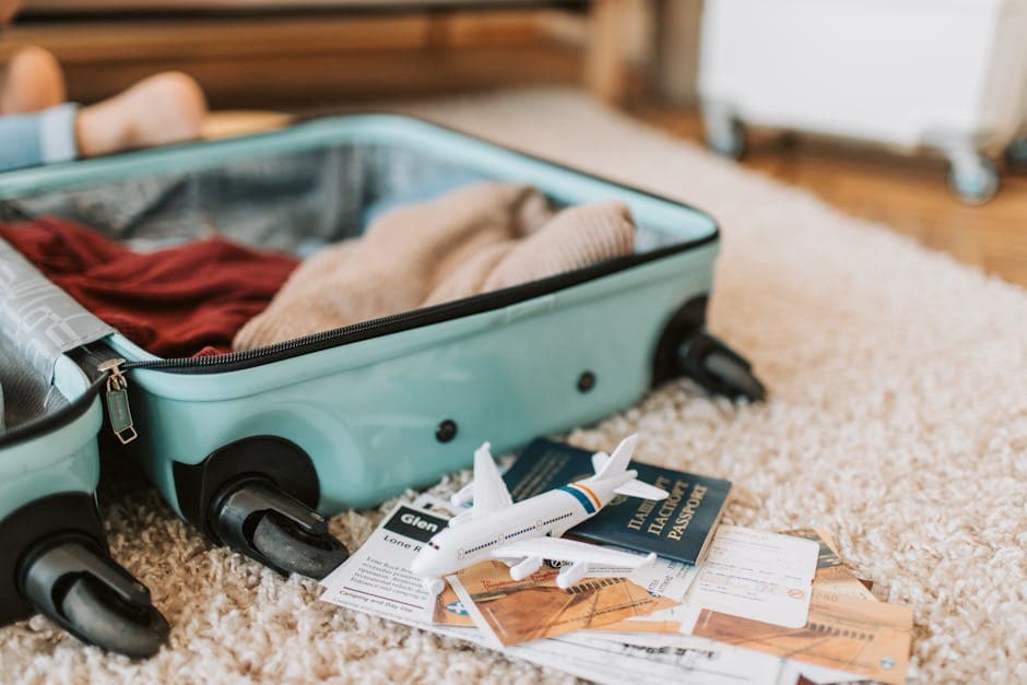 Open teal suitcase with passport tickets and toy plane on rug