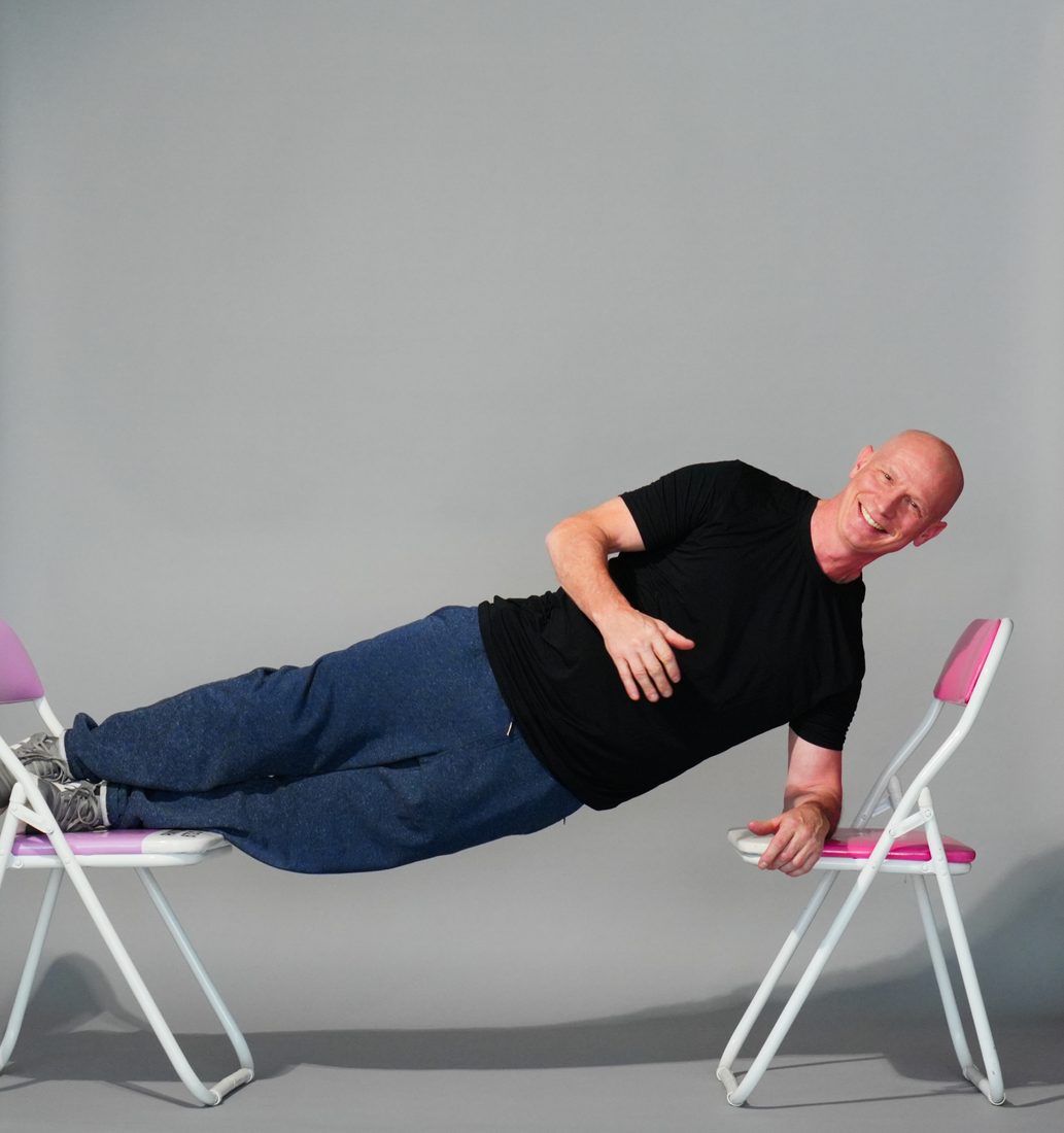 Peter Milhous holding a side plank suspended between two chairs